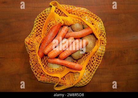 Orangefarbener Netzbeutel. Blick von oben. Frisches Gemüse vom Bauernmarkt. Rohe Kartoffeln, rohe Karotten. Bewusster Konsum, wiederverwendbarer Beutel, Fadenbeutel Stockfoto