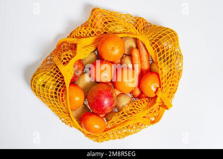 Orangefarbener Netzbeutel. Blick von oben. Frisches Gemüse und Obst vom Bauernmarkt. Rohe Kartoffeln, rohe Karotten, Äpfel, Mandarinen, Orangen. Consci Stockfoto