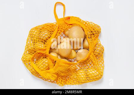 Vernetzen Sie den wiederverwendbaren Beutel mit frischen Kartoffeln. Orangefarbene Tasche mit Schnur. Rohe Kartoffeln. Blick von oben. Vegetarier, Rohkost, frisches Gemüse. Bewusster Konsum Stockfoto