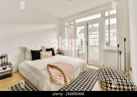 Ein Schlafzimmer mit weißen Wänden und Hartholzfußboden in der Mitte, es gibt einen schwarz-weiß karierten Teppich auf dem Bett Stockfoto