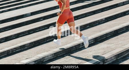 Aktive Frau, die während ihres Treppentrainings die Treppe rauf läuft. Läuferin, die draußen eine Kardioübung macht. Sportliche Frau, die morgens trainiert. Stockfoto