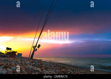 Wunderschöner Sonnenuntergang über dem Meer. Angelruten am Ufer des Meeres vor dem Hintergrund eines dramatischen Sonnenuntergangs. Stockfoto