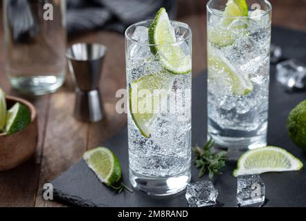 Gin-Tonic-Cocktail mit Limettenscheiben und Eis in einem hohen Glas auf einem schwarzen Schieferbrett Stockfoto