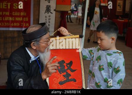 Hanoi, Vietnam. 15. Januar 2023. Ein Kalligraf schreibt ein kalligrafisches Werk für einen Jungen während des Spring Calligraphy Festivals am Van Mieu-Quoc TU Giam (Literaturtempel) in Hanoi, Vietnam, 15. Januar 2023. Das jährliche Frühjahrskalligrafiefest fand am Sonntag in der vietnamesischen Hauptstadt Hanoi statt, nachdem die COVID-19-Pandemie zwei Jahre zurückliegt. Es ist eine lokale Tradition, kalligraphische Werke auf rotem Papier zu haben, die während des Mondneujahrs ausgestellt werden, um für das gute im neuen Jahr zu beten. Kredit: Hu Jiali/Xinhua/Alamy Live News Stockfoto