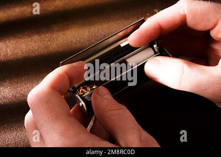 Handgedrehte Zigarette, Rollmaschine, verstreuter Tabak auf dem Hintergrund, Zigarettenrolle mit Filter, Zigarettenfilter. Stockfoto