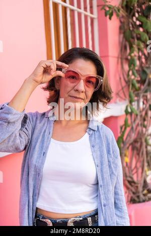 Eine Frau, die die Sonnenbrille anpasst und in die Kamera schaut Stockfoto