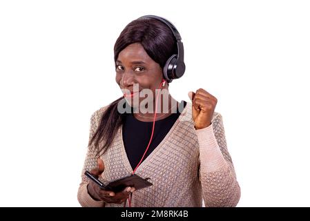 Porträt einer schönen erwachsenen Frau, die mit einem lächelnden Mobiltelefon Musik über Kopfhörer hört. Stockfoto