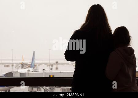 Frau und Kind am Flughafen, die durch das Fenster auf Flugzeuge schauen Stockfoto