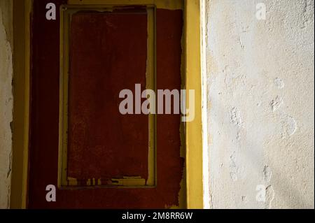 Antike venezianische rote Holztür mit ockerfarbener Verzierung an einer Stuckwand. Stockfoto