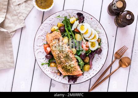 Ein Blick von oben auf einen Lachs-Nicoise-Salat auf einem rustikalen Tisch, bereit zum Essen. Stockfoto
