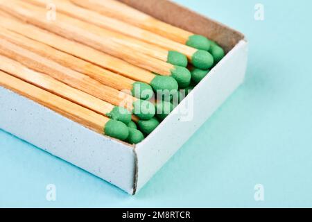 Viele Streichhölzer mit grünen Köpfen in einer Streichholzschachtel auf blauem Hintergrund mit Kopierraum Stockfoto