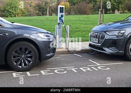 Tesla und Aidi Elektroautos werden an der Ladestation am Straßenrand aufgeladen Stockfoto