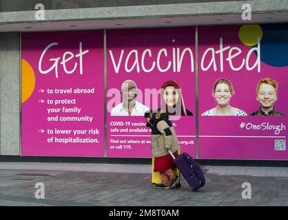 Slough, Berkshire, Großbritannien. 15. Januar 2023. Eine obdachlose Frau geht an einem Schild vorbei, auf dem man geimpft wird, in der Slough High Street. Eine neue Variante des Covid-19 XBB.1,5, bekannt als Kraken, tritt jetzt in Tests in Großbritannien auf. Menschen werden immer noch geraten, ihre Covid-19-Auffrischimpfstoffe zu erhalten. Die Zahl der Menschen mit positiven Covid-19-Tests während der Weihnachtszeit stieg wieder an. Kredit: Maureen McLean/Alamy Live News Stockfoto