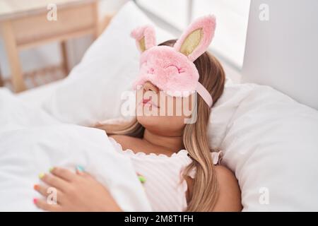 Junge schöne hispanische Frau trägt Schlafmaske auf dem Bett liegend schlafen im Schlafzimmer Stockfoto