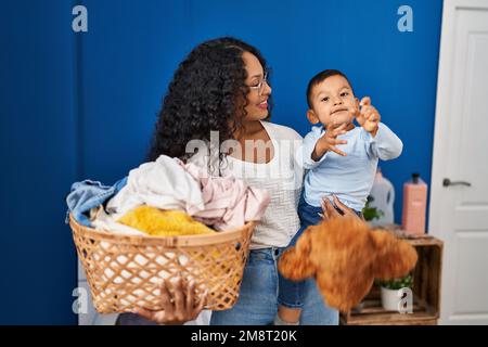 Mutter und Sohn spielen mit Teddybär und warten auf Waschmaschine in der Waschküche Stockfoto