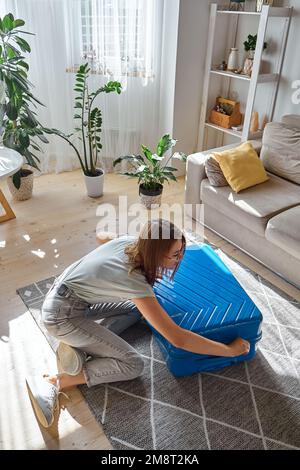 Junge glückliche Frau, die auf Reisen ihren Koffer packt oder auspackt Stockfoto