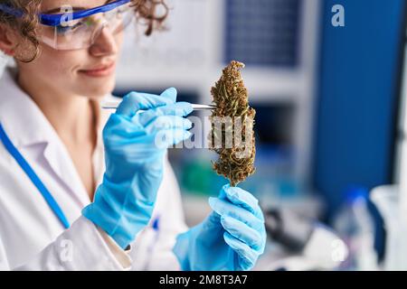 Junge hispanische Wissenschaftlerin hält Marihuana-Pflanze mit Pinzette im Labor Stockfoto