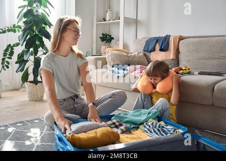 Familienmutter und -Kind, die zusammen einen Koffer und ein Reisekissen packen, um eine Reise oder einen Urlaub zu machen Stockfoto