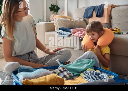 Familienmutter und -Kind, die zusammen einen Koffer und ein Reisekissen packen, um eine Reise oder einen Urlaub zu machen Stockfoto