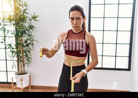 Junge hispanische Frau, die Sportkleidung mit Maßband im Sportzentrum trägt, depressiv und besorgt wegen Not, weinend wütend und ängstlich. Trauriger Ausdruck. Stockfoto