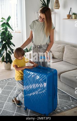 Familienmutter und -Kind verlassen das Haus mit einem Koffer auf eine Reise oder Urlaub Stockfoto