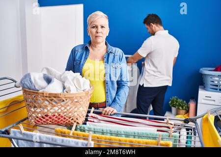 Hispanische Mutter und Sohn hängen Kleider an der Wäscheleine, denken und nüchtern aussehen selbstbewusst Stockfoto