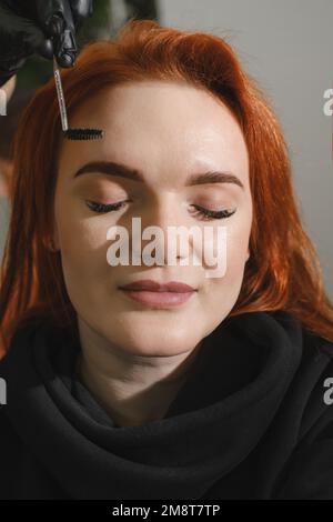 Augenbrauen-Make-up. Gesichtsaufnahme einer schönen Frau mit Augenbrauenkorrektur im Schönheitssalon. Kosmetikerin färbt Augenbrauen für Weibchen. Schönheitsbehandlung Stockfoto