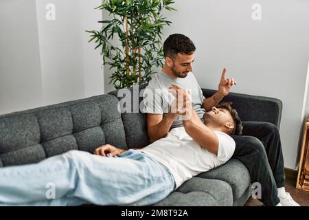 Zwei hispanische Männer, die zu Hause lächeln und selbstbewusst auf dem Sofa sitzen Stockfoto
