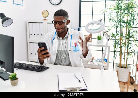 Junger afroamerikanischer Mann in Arztuniform mit Videoanruf in der Klinik Stockfoto