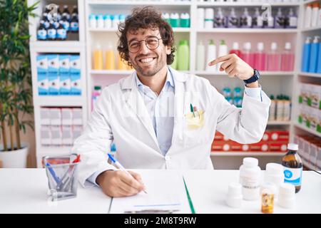 Hispanischer junger Mann, der in einer Apotheke arbeitet, sieht selbstbewusst aus mit einem Lächeln im Gesicht, zeigt sich mit den Fingern stolz und glücklich. Stockfoto