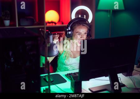 Junge schöne hispanische Frau streamer spielen Videospiel mit Sieger Ausdruck in Gaming-Raum Stockfoto