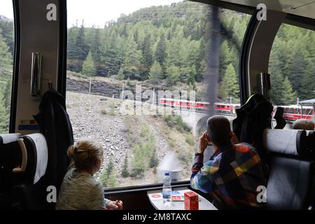 Blick aus dem Inneren des Bernina Express, während der Zug eine Kurve fährt und den Berg, die Alpen, die Schweiz hinaufklettert Stockfoto