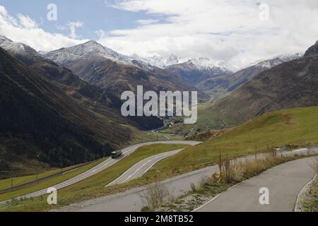 Mit Blick auf ein Tal in den Alpen mit einer Haarnadelstraße und schneebedeckten Bergen in der Ferne, Schweiz Stockfoto