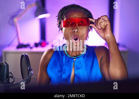 Eine afrikanische Frau mit Dreadlocks, die Videospiele spielt, die eine Virtual-Reality-Brille trägt, verängstigt und verblüfft mit offenem Mund für Überraschung, Ungläubigkeit Gesicht Stockfoto