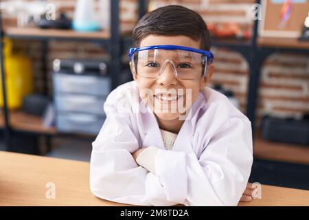 Ein süßer spanischer Schüler, der sich auf den Tisch lehnt, mit den Armen gekreuzten Gesten im Labor Stockfoto