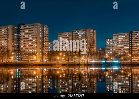 Nachtsicht auf Tysiaclecie Anwesen in Kattowitz, Schlesien, Polen. Leichte Wohngebäude mit umliegenden Bäumen in der Dämmerung, die durch den See gesehen werden. Stockfoto