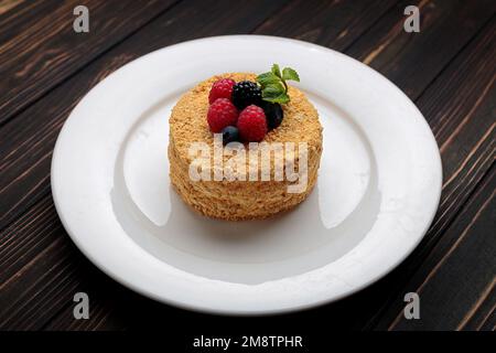 Napoleonkuchen mit Beeren und Minze, auf einem Teller, auf einem Holzhintergrund Stockfoto