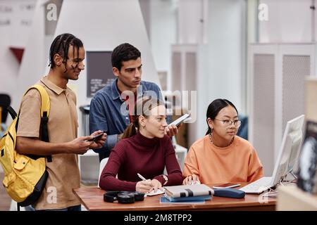 Multiethnische Gruppe von Jugendlichen, die in einer Hochschulbibliothek studieren und Computer gemeinsam nutzen Stockfoto