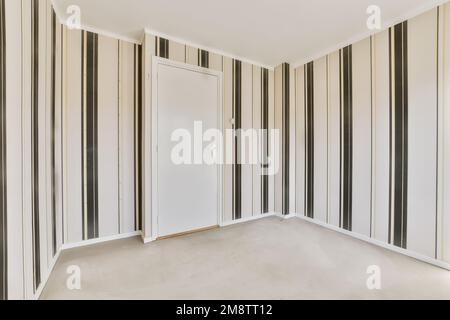 Ein leerer Raum mit schwarz-weiß gestreiften Tapeten an den Wänden und eine Tür in der Ecke Stockfoto