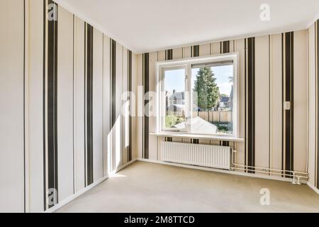 Ein leerer Raum mit gestreiften Tapeten an den Wänden und großen Fenstern im Raum ist weiß, beige und schwarz Stockfoto