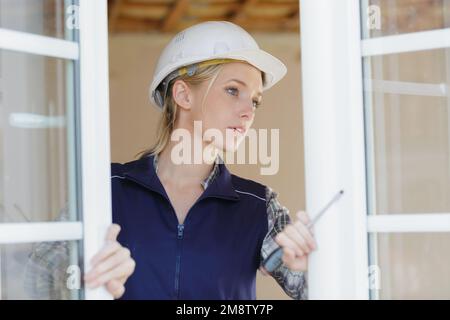 Eine Frau, die einen Schraubenzieher am pvc-Fenster hält Stockfoto