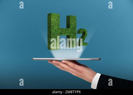 Ein Mann hält eine digitale Tafel mit dem Symbol für Wasserstoff H2 aus Gras Stockfoto