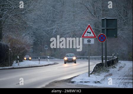 Autos, die im Winter auf einer nassen Straße fahren, mit einer rutschigen Straße und einem Eiswarnschild Stockfoto