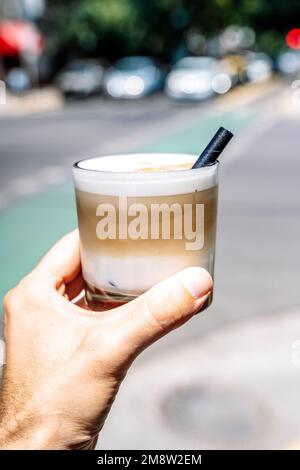 Eine Tasse Latte Cappuccino in der Hand auf der Straße der Stadt. Kaffeegetränk zum Mitnehmen. Hochwertiges Foto Stockfoto