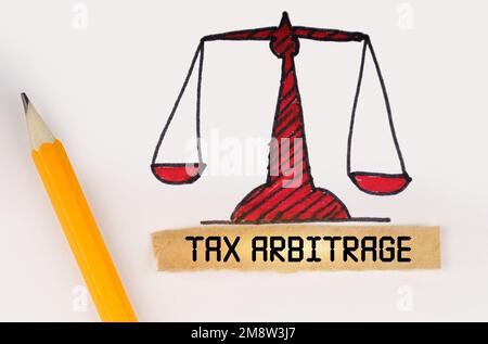 Rechtsbegriff. Neben der bemalten Waage der Gerechtigkeit liegen ein Bleistift und ein Streifen Papier mit der Inschrift "Tax Arbitrage" Stockfoto