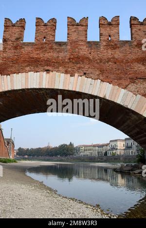 Mittelalterliche Steinbrücke über einen flachen Fluss aus rotem Ziegelstein. Darunter sind die Häuser der Stadt in der Ferne zu sehen Stockfoto