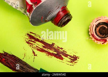 Roter Künstler Ölfarbe mit Pinsel und Rohr auf grünem Hintergrund Stockfoto