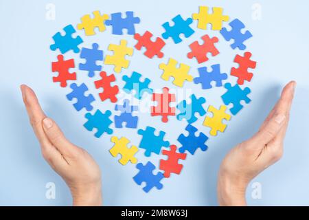 Weltautismus-Sensibilisierungstag-Konzept. Frauenhände mit farbenfrohem Puzzleherz auf hellblauem Hintergrund. Draufsicht, Kopierbereich Stockfoto
