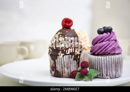 Bunte Cupcakes mit Sahne-Zuckerguss und Beeren. Heidelbeeren und Schokoladen-Cupcakes. Dekoriertes Dessert. Stockfoto