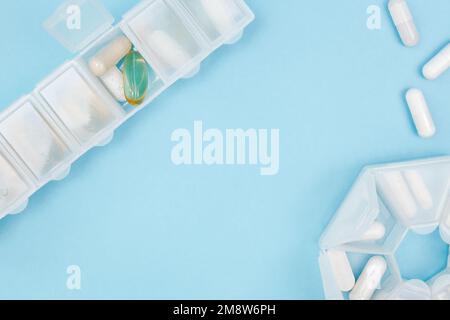 Pillen-Organisator mit einer Vielzahl von Pillen und Ergänzung. Wöchentlicher Tablettenorganisator oder tägliche Tablettenschachtel mit Medikamenten auf blauem Hintergrund. Kopierbereich, Abstand für Stockfoto